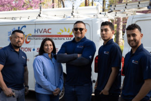 5 members of the crew at JC&JC HVAC Mechanical Contractors standing in front of the company's vehicles.