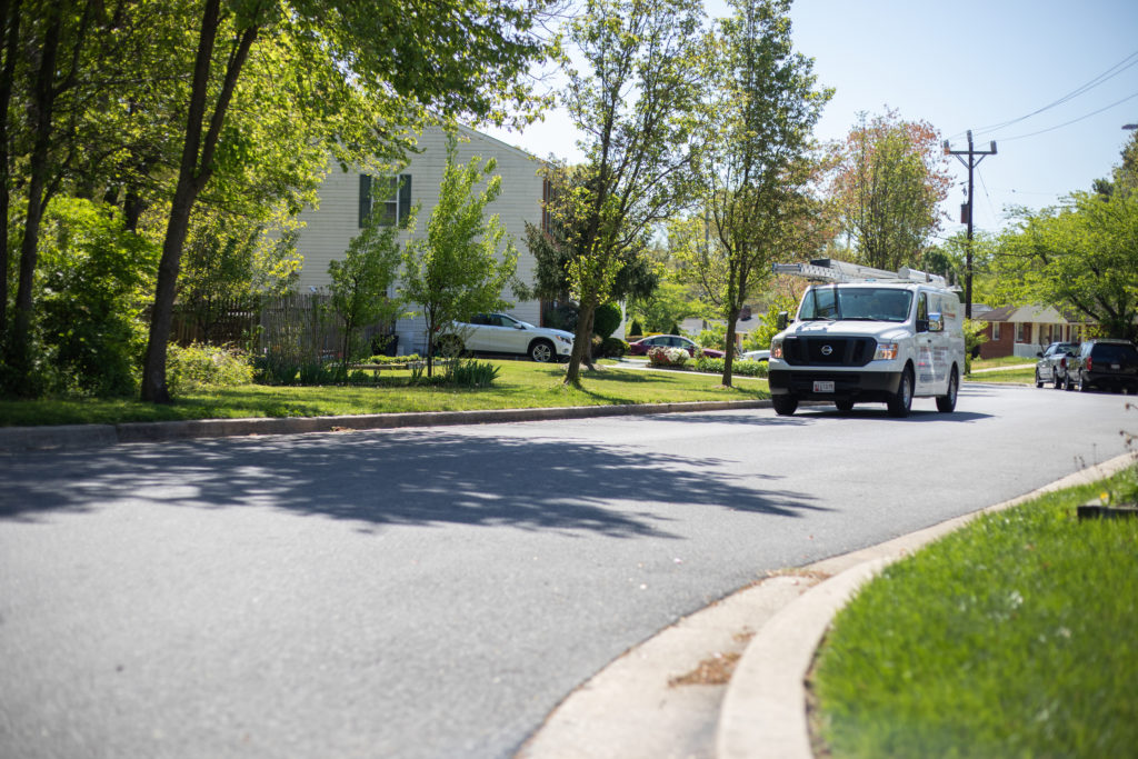 A white service truck driving through a neighborhood with green grass and trees.