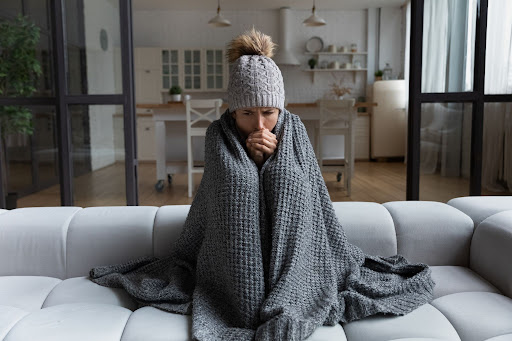 A woman looking cold with a blanket on her as she sits on a couch.