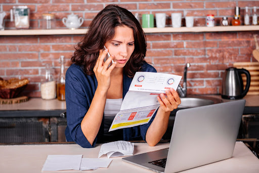 concerned woman on phone holding utility bill in front of laptop