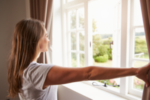 woman opening curtains and looking out window